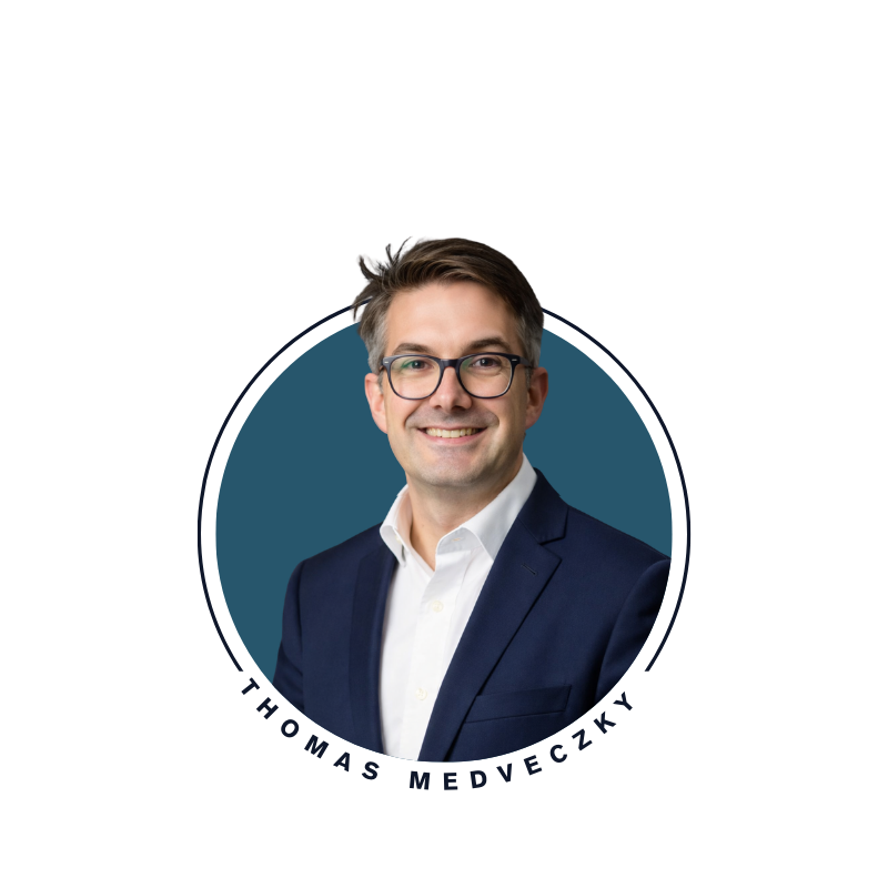 Portrait of Thomas Medveczky wearing glasses and a navy suit, smiling.